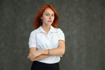 Photo Portrait of a cute girl woman with bright red hair manager in a white shirt on a gray background in the studio. He talks, shows his hands in front of the camera with emotions.