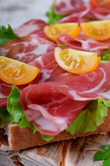 Close-up of thin slices of Italian cold cut pork Coppa on slices of grain bread with salad leaves and cherry tomatoes