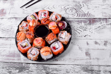 Sushi rolls assortment and soy sauce served on round plate on white wooden table