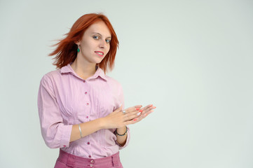 Photo Portrait of a cute girl woman with bright red hair manager in a pink shirt on a white background in studio. He talks, shows his hands in front of the camera with emotions.