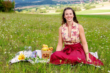 young brunette woman in dirndl sitting in a field of flowers on a blanket