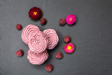 Fototapeta na wymiar Fresh organic homemade zephyr or marshmallows decorated by flowers on black textured background.