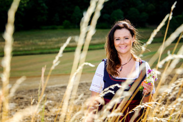 brunette woman in dirndl standing outdoors and holding flowers