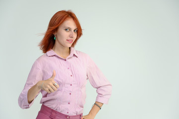 Obraz premium Photo Portrait of a cute girl woman with bright red hair manager in a pink shirt on a white background in studio. He talks, shows his hands in front of the camera with emotions.