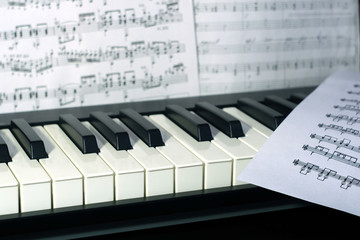 Music keyboard with pages with music notes close up view, selective focus