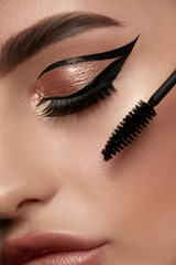 close-up of woman eye with luxury golden make-up and mascara brush