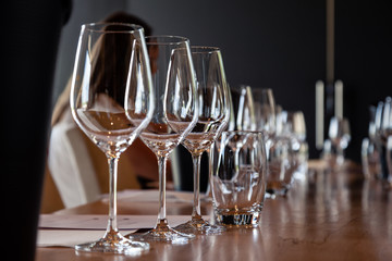 Closeup empty clear transparent crystal wine and water glasses standing on table in straight rows on wine tasting. Concept modern setting on background professional degustation with sommelier