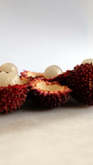 Obraz na płótnie Canvas Peeled pulasan fruits in vertical photo. Scientific name Nephelium ramboutan-akea, pulasan is a red tropical fruit that is closely allied to rambutan and sometimes confused with it.