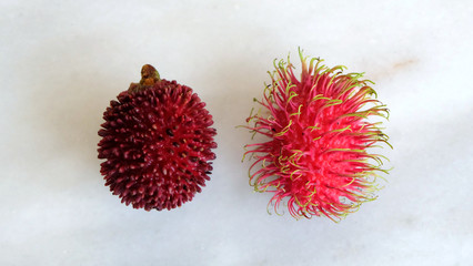 Pulasan and rambutan fruits arranged side by side. Both are tropical fruits from southeast Asia, and are sometimes confused for one another because they look similar.