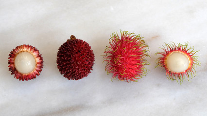 Top view of pulasan and rambutan fruit, arranged side by side. Both are tropical fruits from southeast Asia, and sometimes confused for one another because they look similar.