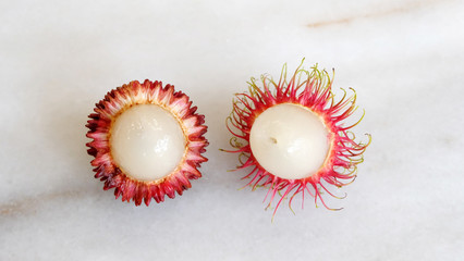 Pulasan and rambutan with the skin peeled off and the white inner flesh visible, arranged side by side. Both are tropical fruits from southeast Asia, and sometimes confused for one another.
