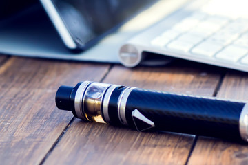 A vaporizer and laptop are on the wooden table. Smoke devise