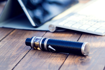 A vaporizer and laptop are on the wooden table. Smoke devise