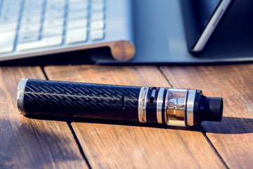 A vaporizer and laptop are on the wooden table. Smoke devise