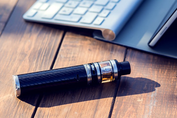 A vaporizer and laptop are on the wooden table. Smoke devise