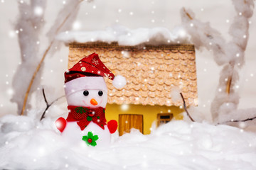 Toy snowman near home during snowfall. Christmas card_