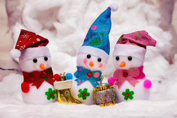 Three funny toy snowmen with Christmas decorations and gifts in the snow. Christmas card_