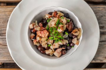 gray peas with smoked meats and fried onions, garnished with green onions in a porcelain bowl on a wooden table. Latvian cuisine, christmas dish
