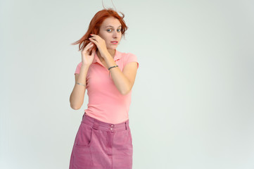 Photo Portrait of a cute woman girl with bright red hair in a peach t-shirt and pink skirt on a white background in studio. He talks, shows his hands in front of the camera with emotions.