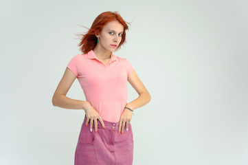 Obraz na płótnie Canvas Photo Portrait of a cute woman girl with bright red hair in a peach t-shirt and pink skirt on a white background in studio. He talks, shows his hands in front of the camera with emotions.