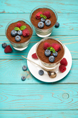 Classic tiramisu dessert with blueberries and strawberries in a glass cup on wooden background