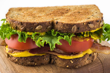 Close up of BLT sandwich with bacon, tomatoes, lettuce and yellow mustard.