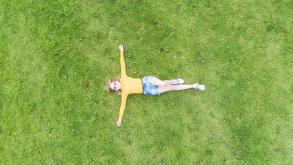 Young girl lying and resting on lawn on sunny day. Top down view. Drone shot. 