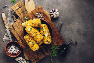 Flat lay sweet corn grilled with cheese, cilantro and spices on a rustic cutting board. Vegetarian,...
