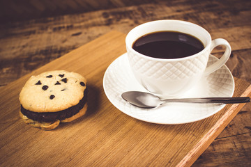 Cookie butter and chocolate Cookies stacked 3 pieces, black coffee in the cup white on white coasters,and stainless steel spoon are on a wooden tray ,  all placed on a wooden table.