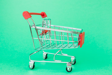 Reduced copy of a shopping cart for supermarkets on a green background. The concept of shopping,...