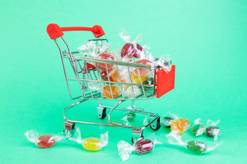 A small copy of a supermarket basket on a green background. Inside - multi-colored caramel dragees....