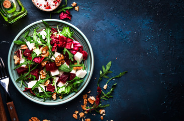 Arugula, Beet and cheese salad with fresh radicchio and walnuts on plate with fork, dressing and spices on blue kitchen table background, place for text, top view