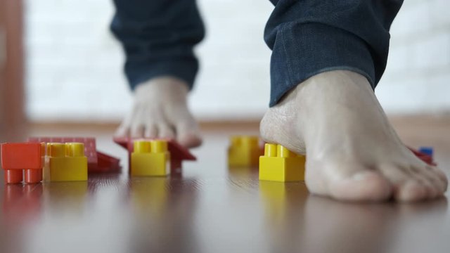 Injury from children's toys. The parent hurts his legs against the construction set scattered on the floor.