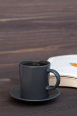 dark cup of coffee with book on wooden table