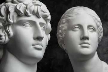 Gypsum copy of ancient statue Antinous and Venus head on dark textured background. Plaster sculpture face.