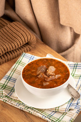 Soup with beef, tomato, potato cabbage and pepper in a cup on a saucer and linen napkin