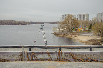 Theodolite measuring instrument stands on a bridge against the background of the city