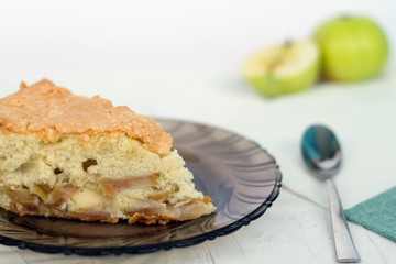 apple pie on a dark glass plate with fresh fruits and spoon on a white background.