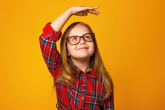 Closeup portrait of a little girl on a yellow background. A child with glasses measures his height.