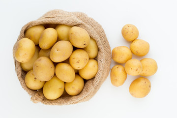 Sack of fresh raw potatoes on wooden background, top view