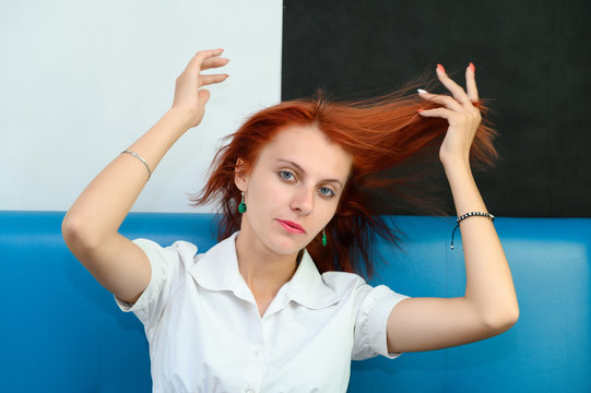 Photo Portrait of a cute woman girl with bright red hair in a white T-shirt on a black and white background in studio. Sits on a blue sofa, Talks in front of the camera with emotions.