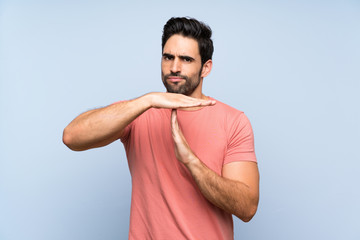 Handsome young man in pink shirt over isolated blue background making time out gesture