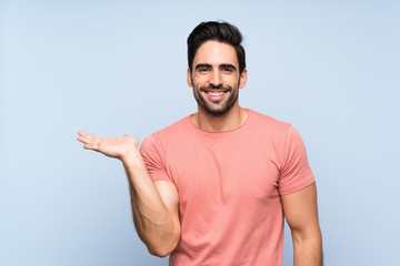 Fototapeta premium Handsome young man in pink shirt over isolated blue background holding copyspace imaginary on the palm to insert an ad