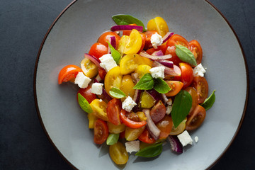 Colorful cherry tomatoes and basil salad in a plate, dark background. Healthy, summer food.