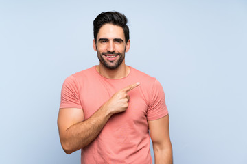 Fototapeta premium Handsome young man in pink shirt over isolated blue background pointing to the side to present a product