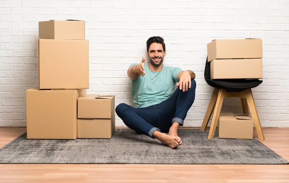 Handsome young man moving in new home among boxes handshaking after good deal