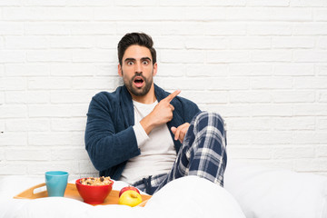 Man in bed with dressing gown and having breakfast surprised and pointing side