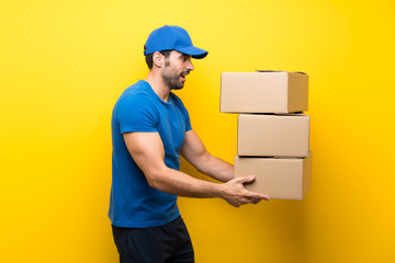 Young delivery man over isolated yellow wall
