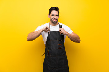 Young hairdresser man over isolated yellow background proud and self-satisfied