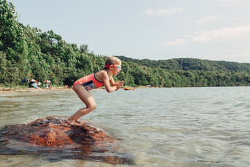 Cute funny Caucasian girl swimming in lake river with underwater goggles. Child diving in water on beach. Authentic real lifestyle happy childhood. Summer fun outdoor aquatic activity.